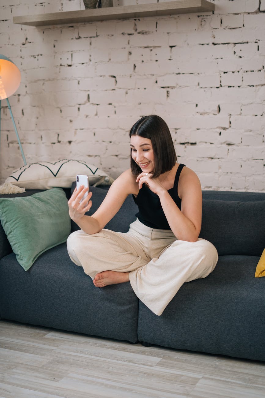 woman in black tank top and white pants sitting on gray couch